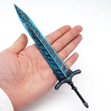 Épée héros elden ring turquoise et noire avec motifs gravés tenue en main dans une collection d’épées elden ring