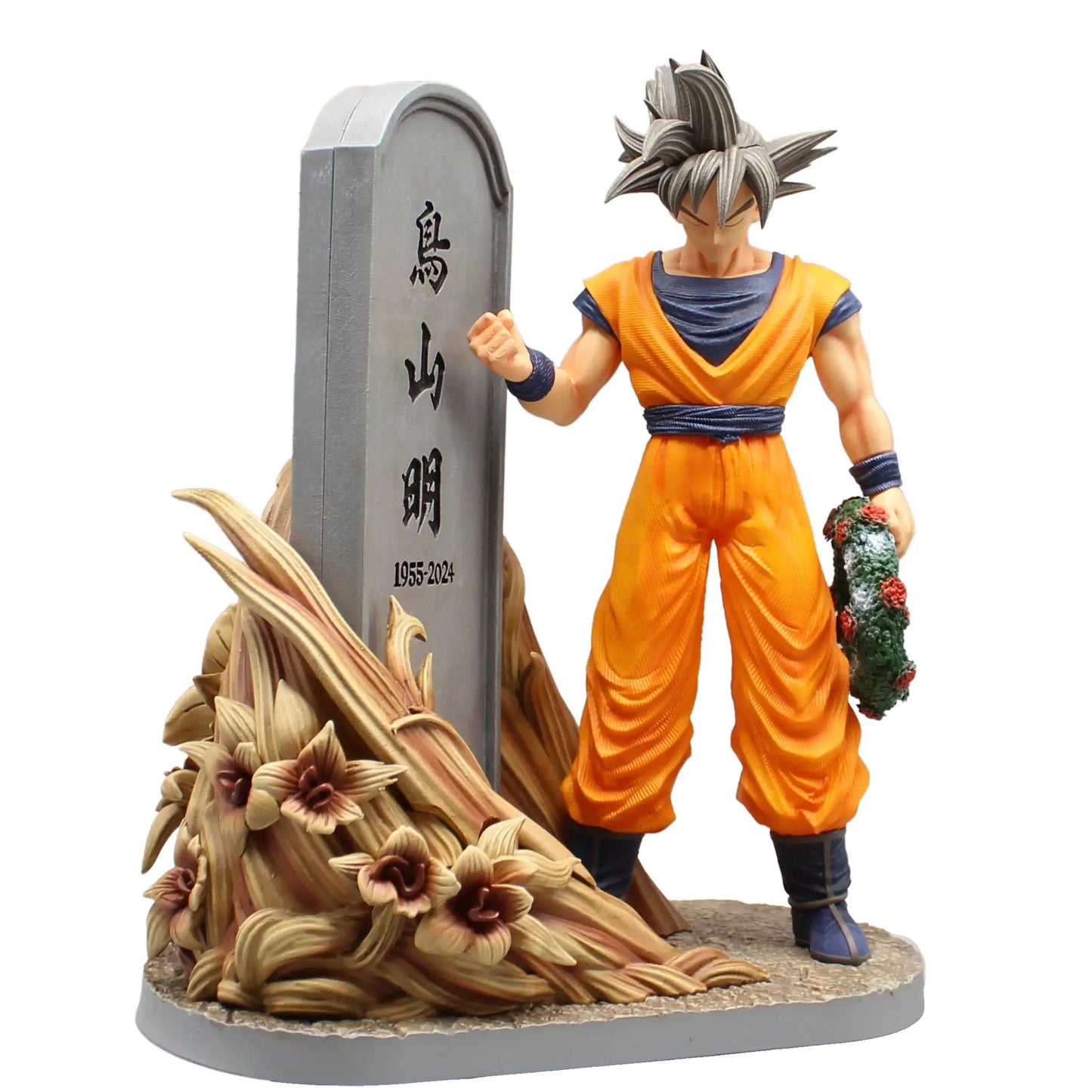 Figurine dragon ball goku orange et bleu rendant hommage à akira toriyama à côté d’une tombe avec un bouquet floral