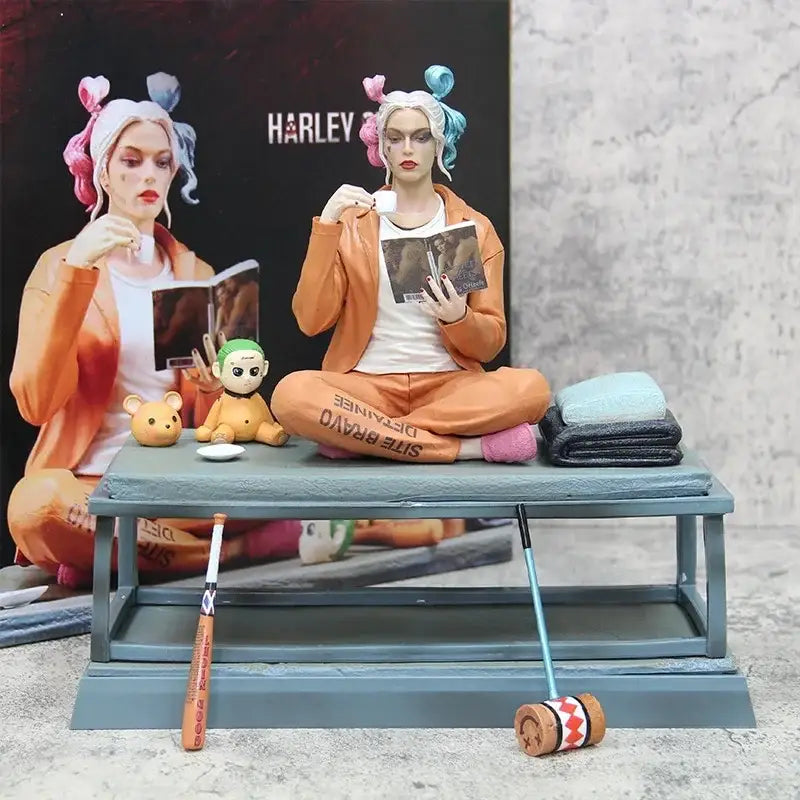 Figurine harley quinn suicide squad en combinaison orange avec pigtails roses et bleus assise en tailleur lisant un livre
