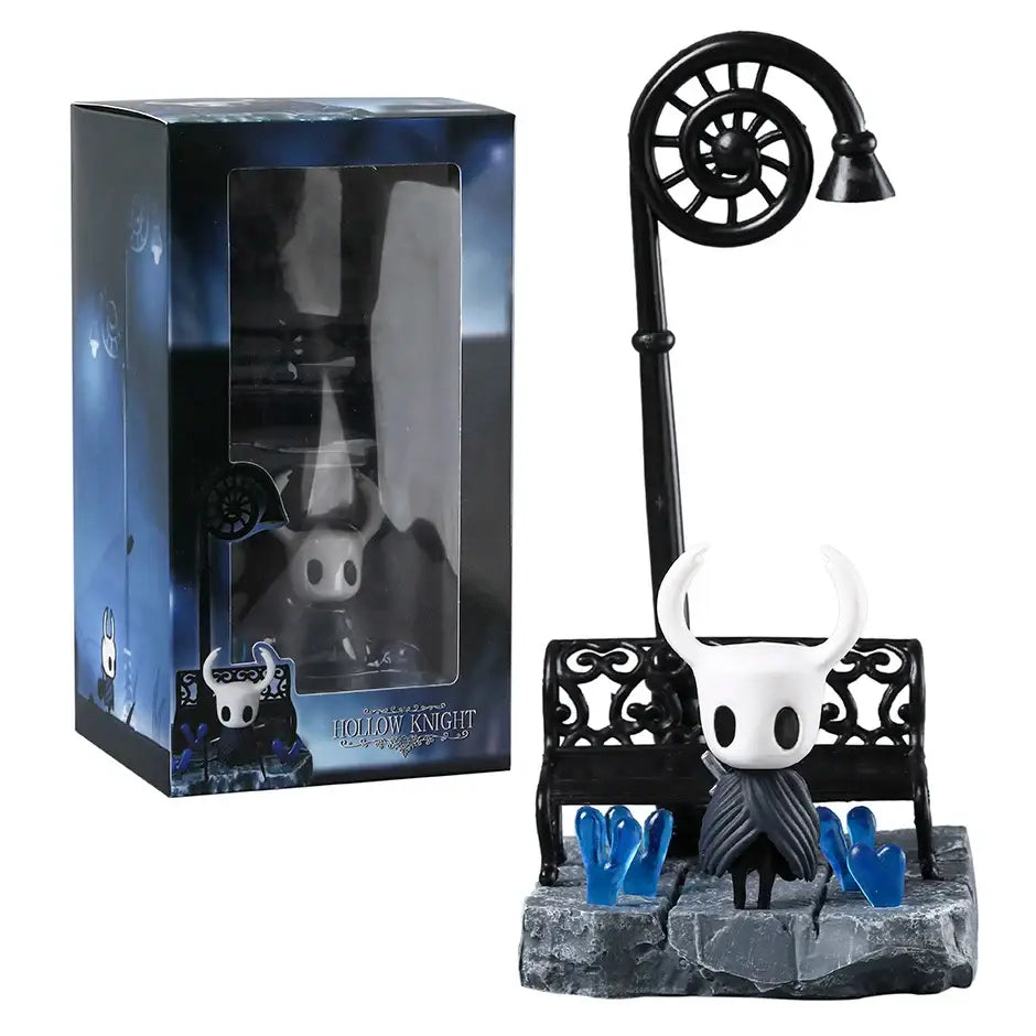 Figurine diorama hollow knight blanc avec cornes noires et cape rayée grise assise sur banc noir orné près de coeurs bleus lumineux