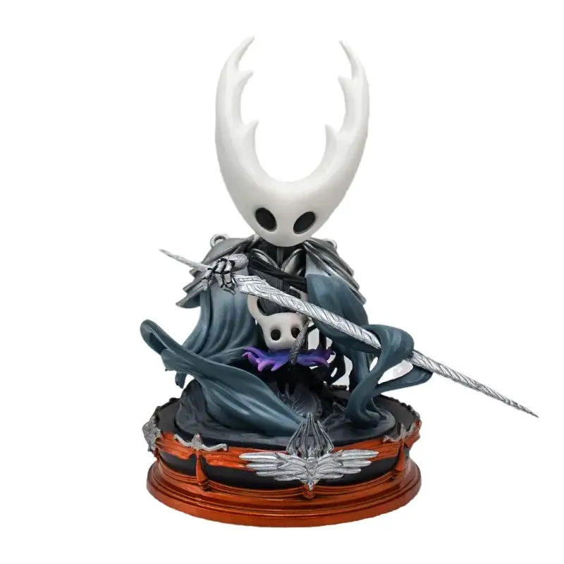 Figurine hollow knight silksong représentant une figure blanche à cornes avec yeux noirs, cape grise et épée argentée sur socle bronze
