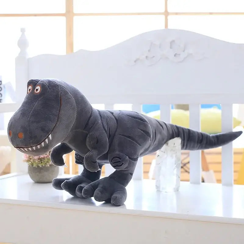 Grande peluche dinosaure mignon noire avec yeux et dents brodés assise sur une surface blanche