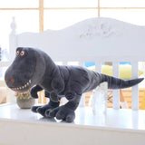 Grande peluche dinosaure mignon noire avec yeux et dents brodés assise sur une surface blanche