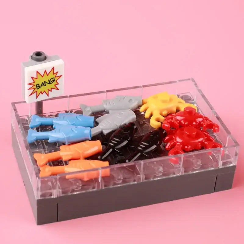 Clear plastic display case with gray base holding colorful lego moc fish and sea creatures including lego legumes and fruits