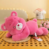 Une peluche bisounours dodo calin rose avec museau blanc et nez en forme de cœur rouge, couchée sur le côté