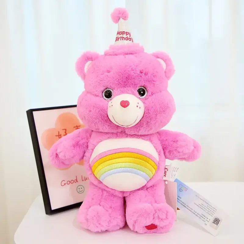 Peluche doudou bisounours calinours rose avec un chapeau de fête blanc et ventre arc-en-ciel rayé avec yeux noirs boutons