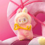 Une peluche labubu pop mart douce et rose avec des accents jaunes tient une clé jaune brillante
