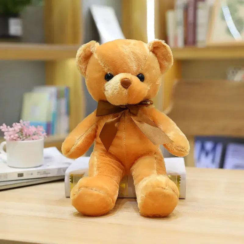 Un peluche teddy bear couleur marron clair avec peluche douce et noeud assorti posé sur des livres