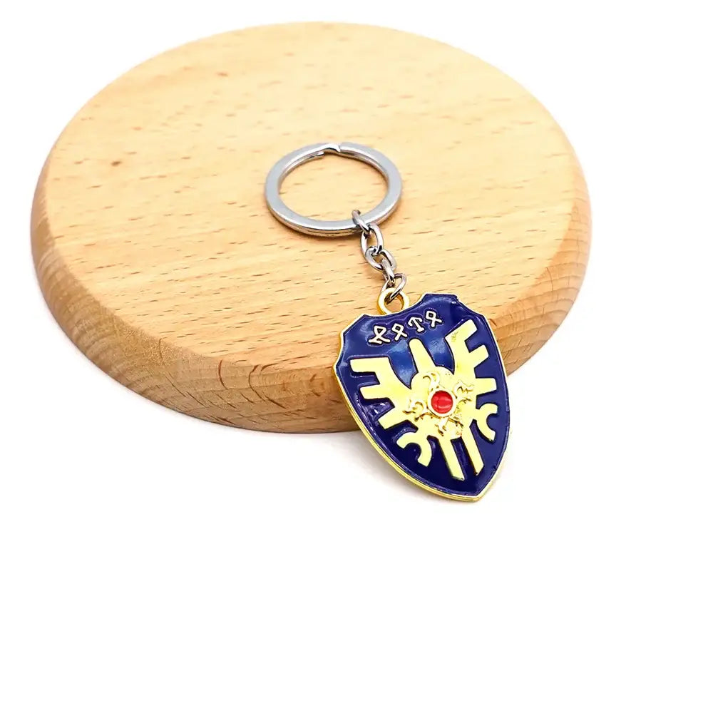 Porte-clé zelda en forme de bouclier bleu et or avec un centre en pierre rouge et un design embossé