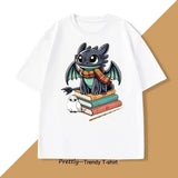 T-shirt anime blanc en coton avec design cartoon de toothless portant une écharpe rayée assis sur des livres avec une chouette
