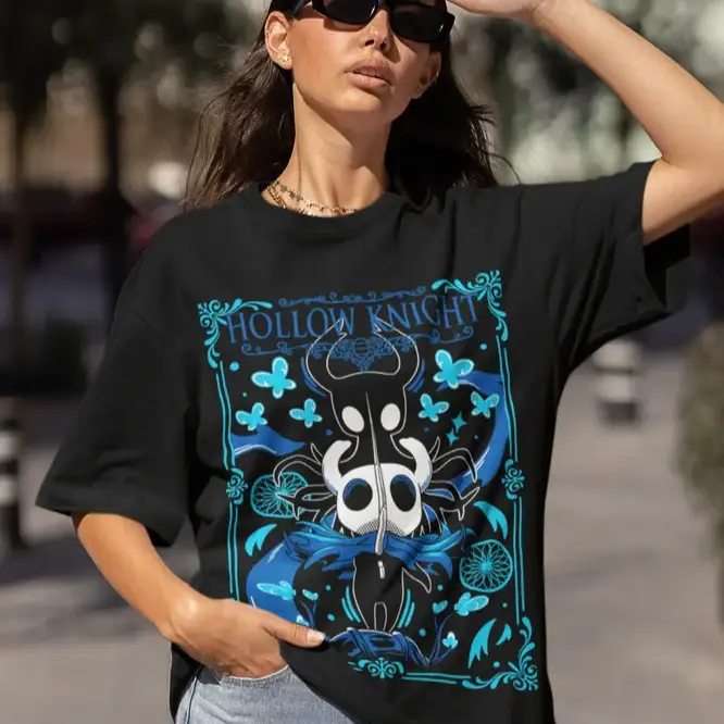 T-shirt hollow knight noir oversize avec design sombre bleu blanc jeu vidéo motifs papillons et bordures ornées