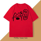 T-shirt unisexe rouge avec un anime chat noir aux yeux larges et texte japonais dans une bulle de dialogue couleurs tendance